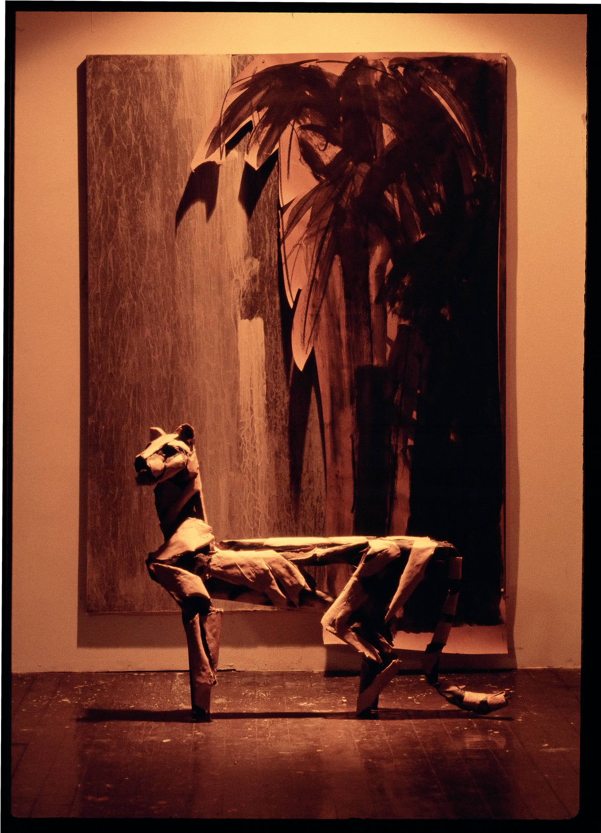 Paper-and-wire lioness sculpture standing on a wood floor before a large painted panel.